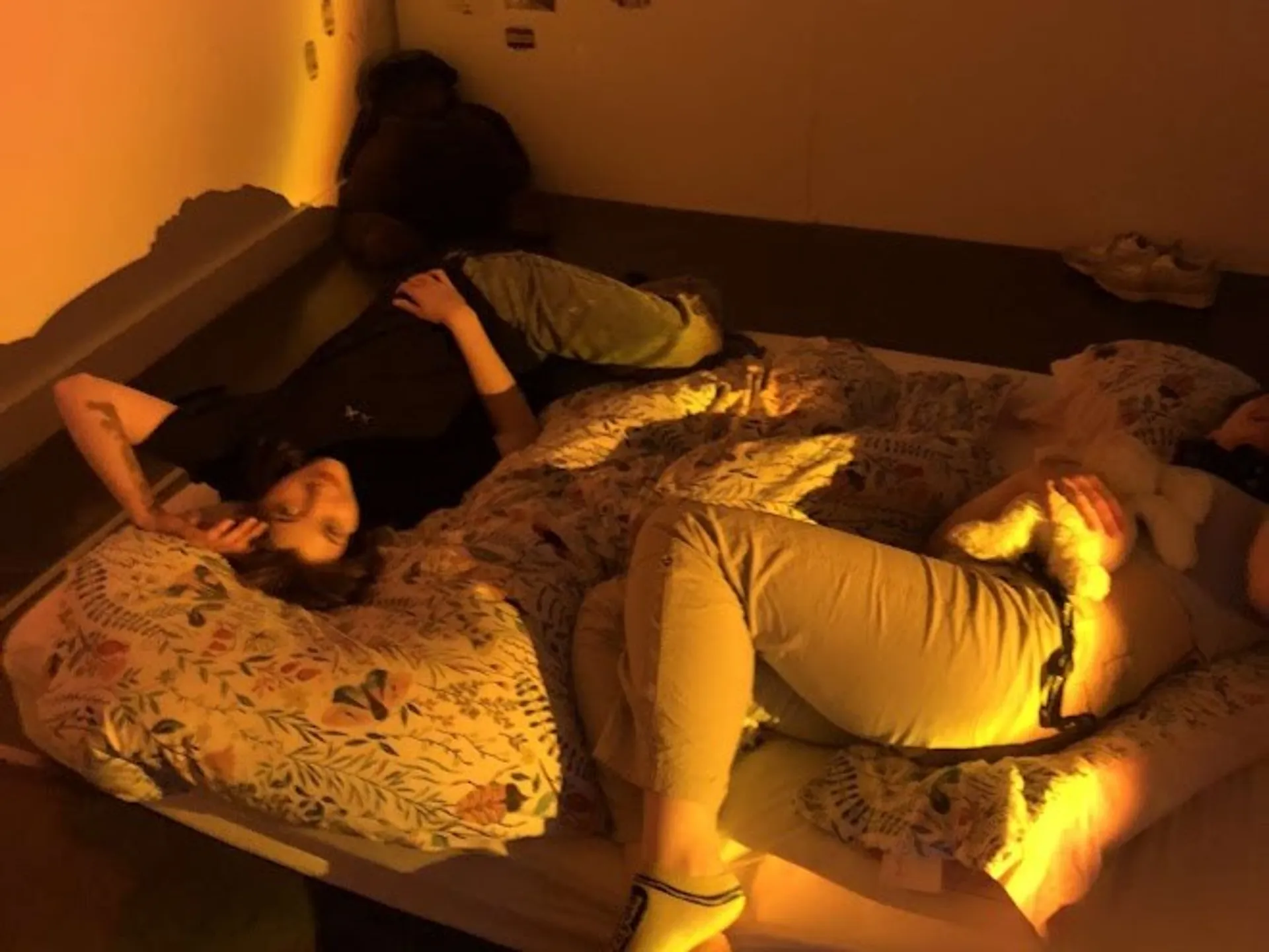 Two people laying on a messy bedspread on the floor under a yellow/orange light.